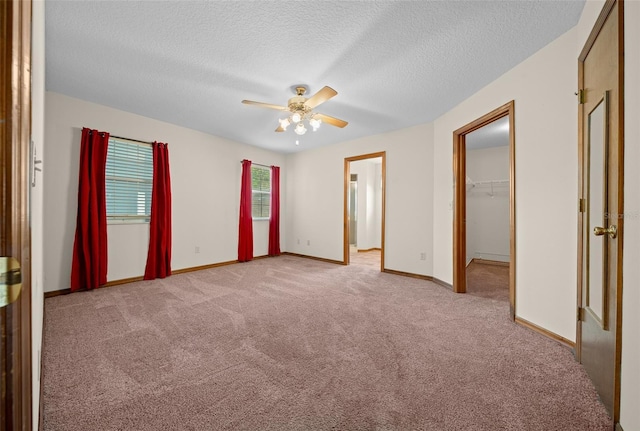 unfurnished bedroom with a spacious closet, ceiling fan, a closet, light colored carpet, and a textured ceiling