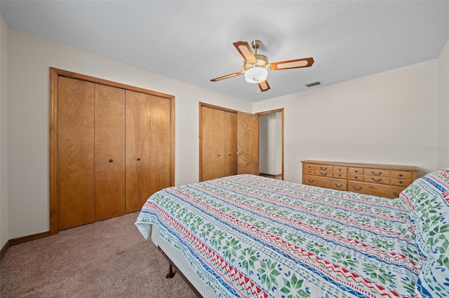 bedroom with ceiling fan, light colored carpet, and multiple closets