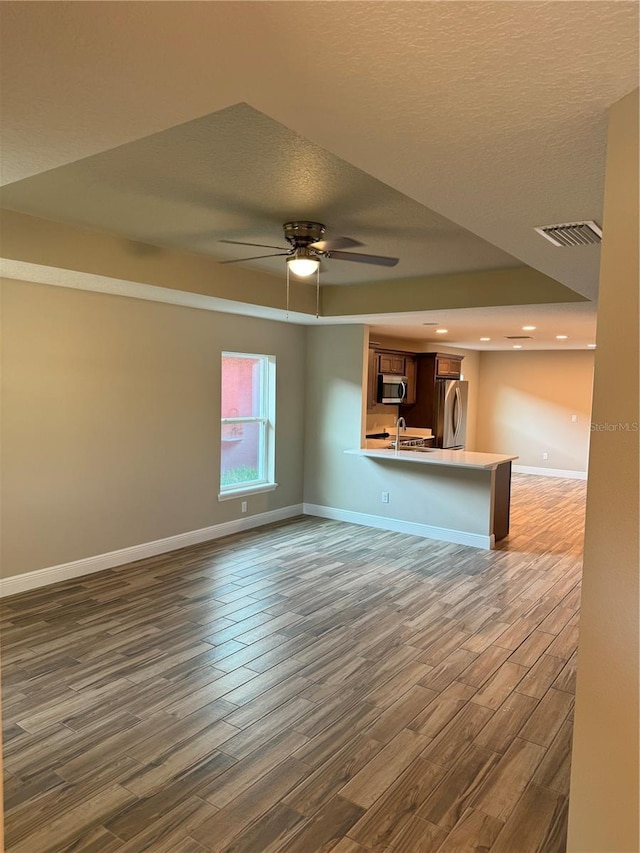 unfurnished living room with dark wood-type flooring, ceiling fan, sink, and a textured ceiling