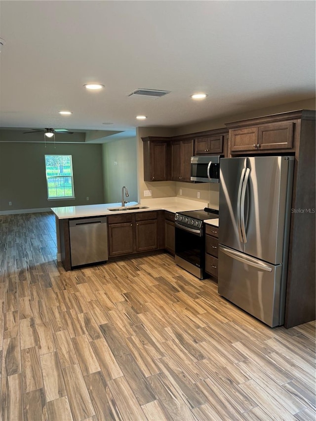 kitchen with sink, light hardwood / wood-style flooring, stainless steel appliances, dark brown cabinetry, and kitchen peninsula