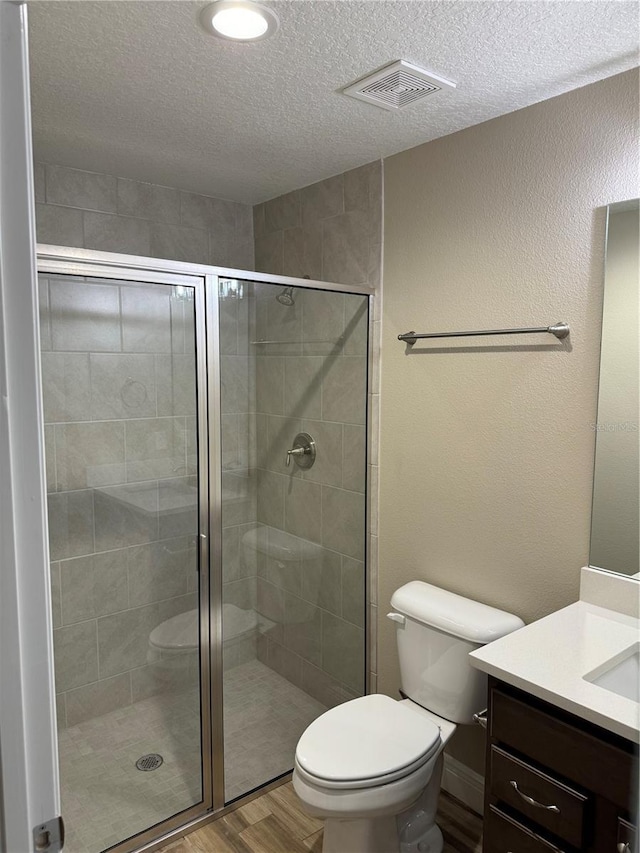 bathroom featuring a shower with door, vanity, wood-type flooring, a textured ceiling, and toilet