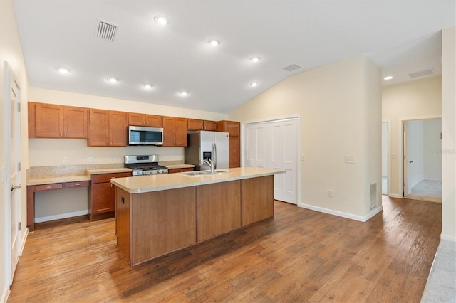 kitchen featuring lofted ceiling, sink, light wood-type flooring, appliances with stainless steel finishes, and a kitchen island with sink