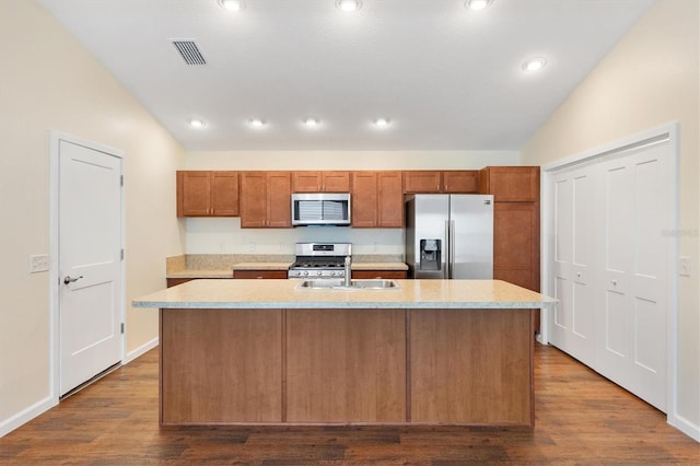 kitchen with vaulted ceiling, stainless steel appliances, an island with sink, and wood-type flooring