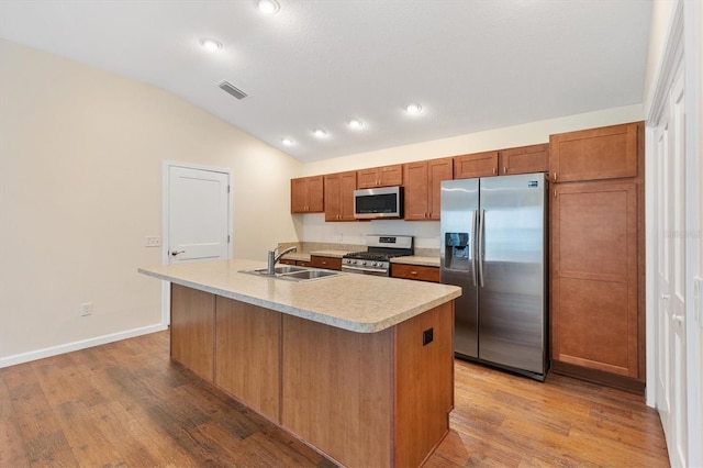 kitchen with lofted ceiling, sink, appliances with stainless steel finishes, light hardwood / wood-style floors, and a center island with sink