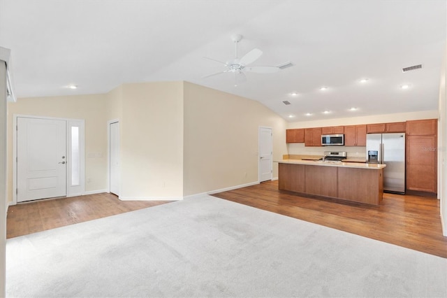 kitchen featuring vaulted ceiling, appliances with stainless steel finishes, ceiling fan, a center island with sink, and light hardwood / wood-style flooring