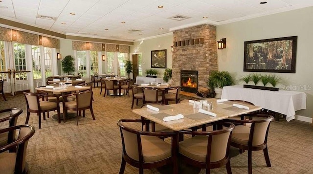 dining room with crown molding, a stone fireplace, and carpet flooring