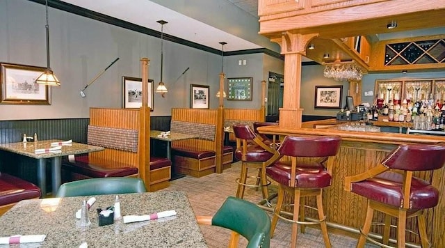 bar with decorative light fixtures, crown molding, ornate columns, and wooden walls