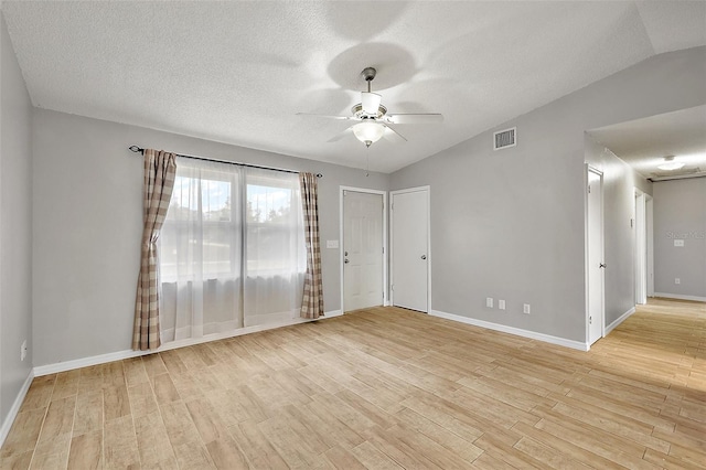 empty room featuring a textured ceiling, light hardwood / wood-style flooring, vaulted ceiling, and ceiling fan