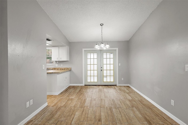 unfurnished dining area with a chandelier, a wealth of natural light, a textured ceiling, and french doors