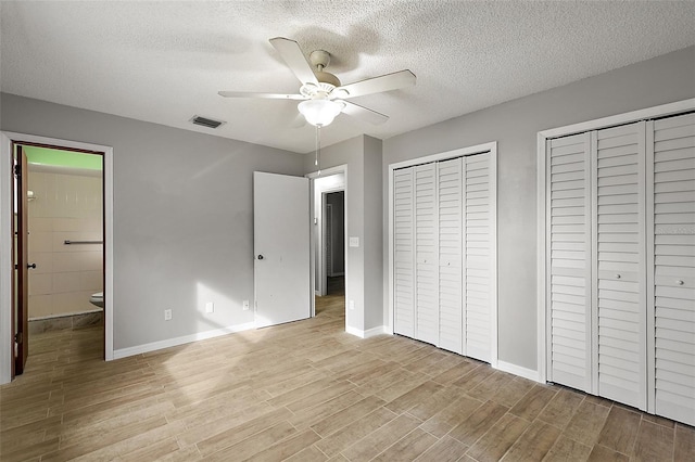 unfurnished bedroom featuring ceiling fan, connected bathroom, a textured ceiling, and multiple closets