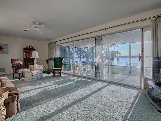 carpeted living room with a water view and ceiling fan