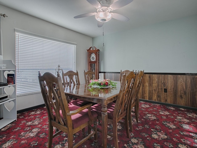 dining area featuring dark carpet, ceiling fan, and wood walls