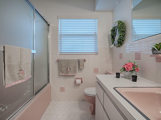 full bathroom featuring combined bath / shower with glass door, tile walls, tile patterned flooring, vanity, and toilet