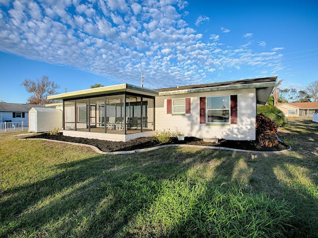 rear view of house featuring a sunroom, a storage unit, and a lawn