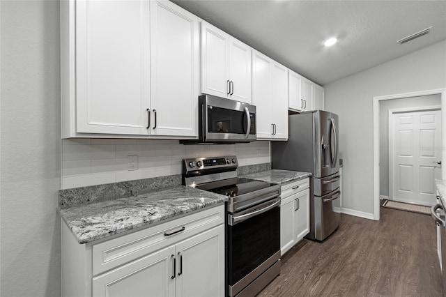 kitchen with vaulted ceiling, dark hardwood / wood-style floors, white cabinetry, light stone counters, and stainless steel appliances