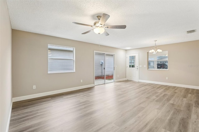 empty room featuring ceiling fan with notable chandelier, a textured ceiling, and light wood-type flooring