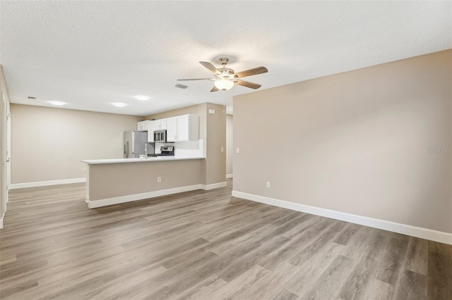 unfurnished living room featuring ceiling fan, a textured ceiling, and light wood-type flooring