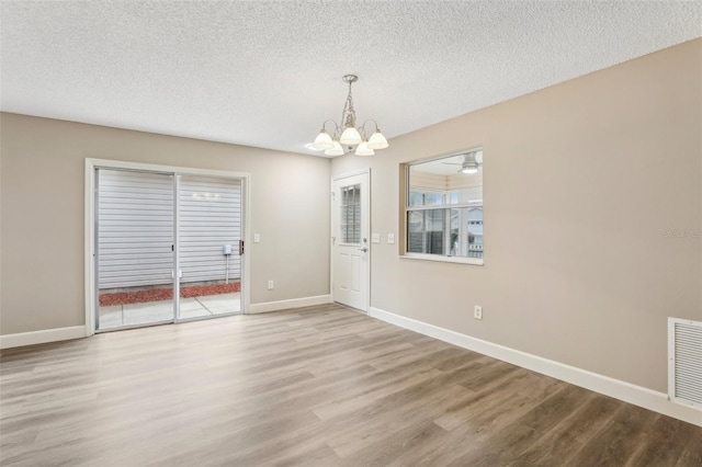 empty room featuring an inviting chandelier, a textured ceiling, and light hardwood / wood-style floors