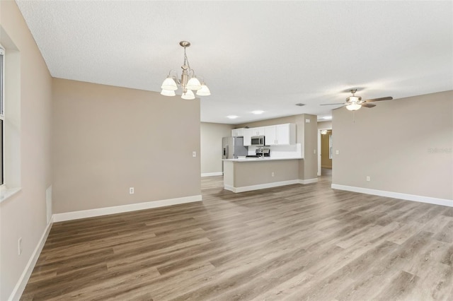 unfurnished living room with ceiling fan with notable chandelier, wood-type flooring, and a textured ceiling