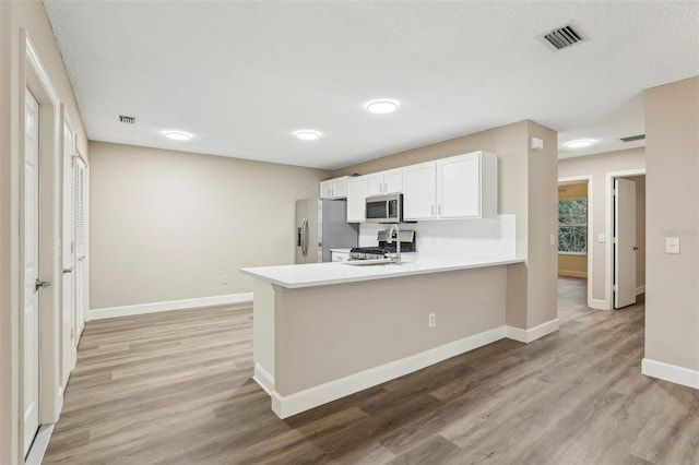 kitchen featuring white cabinetry, stainless steel appliances, kitchen peninsula, and light wood-type flooring