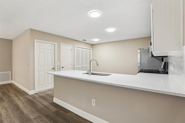 kitchen with sink, dark wood-type flooring, stove, decorative backsplash, and kitchen peninsula