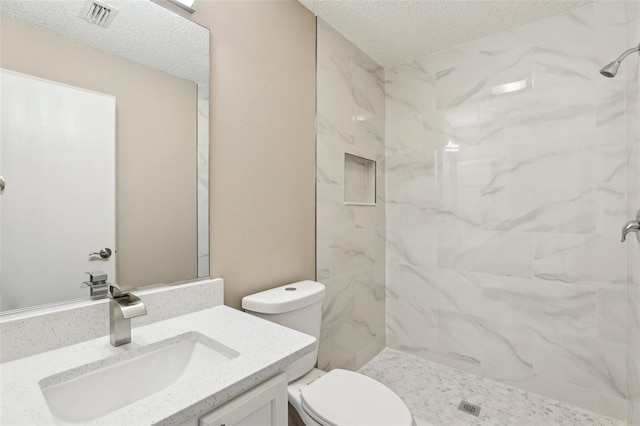 bathroom with vanity, tiled shower, a textured ceiling, and toilet