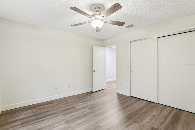 unfurnished bedroom with ceiling fan, a textured ceiling, light hardwood / wood-style floors, and a closet