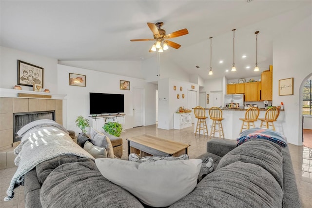 living room featuring ceiling fan, high vaulted ceiling, light tile patterned floors, and a tiled fireplace