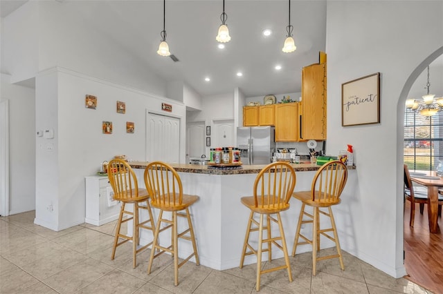 kitchen with kitchen peninsula, stainless steel refrigerator with ice dispenser, light tile patterned floors, a kitchen bar, and high vaulted ceiling