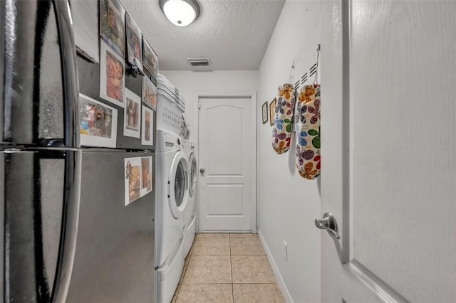 clothes washing area with washing machine and clothes dryer, light tile patterned floors, and a textured ceiling