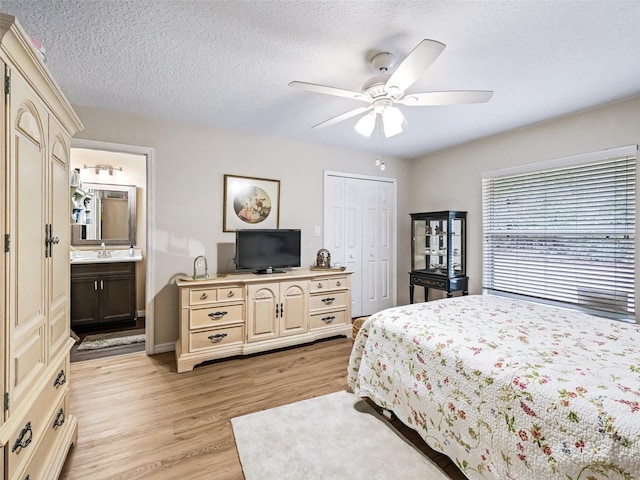 bedroom with ensuite bathroom, a textured ceiling, light hardwood / wood-style flooring, a closet, and ceiling fan