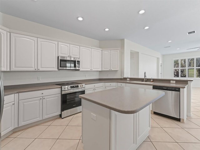 kitchen featuring sink, light tile patterned floors, stainless steel appliances, white cabinets, and a kitchen island