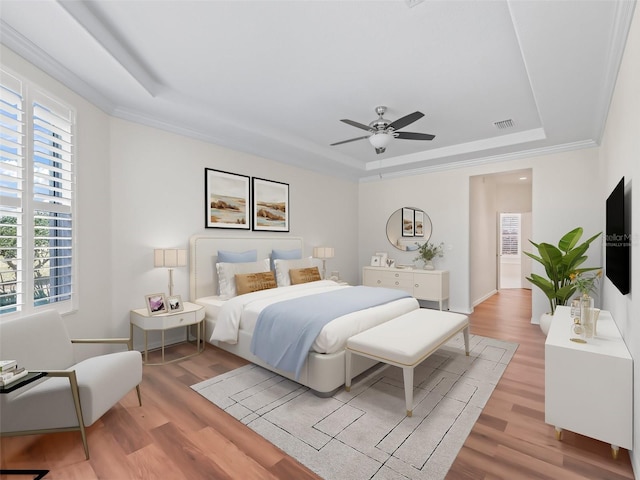 bedroom featuring ceiling fan, ornamental molding, a raised ceiling, and light hardwood / wood-style flooring