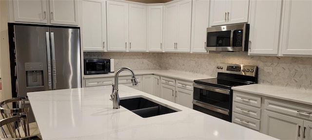 kitchen with sink, white cabinetry, a kitchen breakfast bar, stainless steel appliances, and light stone countertops