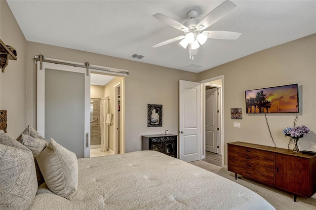 bedroom featuring light carpet, a barn door, visible vents, a ceiling fan, and ensuite bath