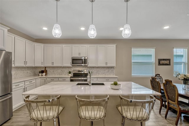 kitchen with an island with sink, white cabinetry, appliances with stainless steel finishes, and decorative light fixtures