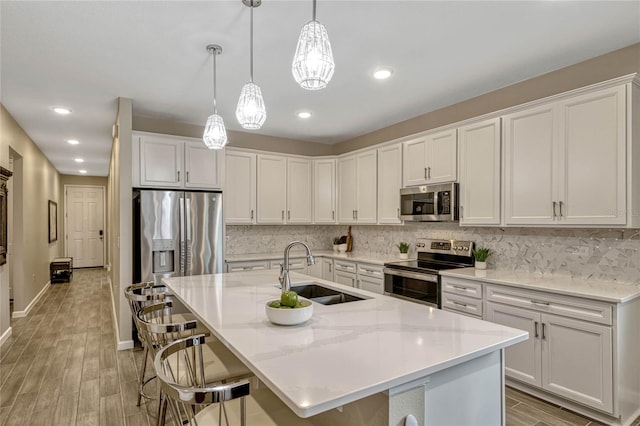 kitchen with a kitchen island with sink, a sink, white cabinetry, hanging light fixtures, and appliances with stainless steel finishes