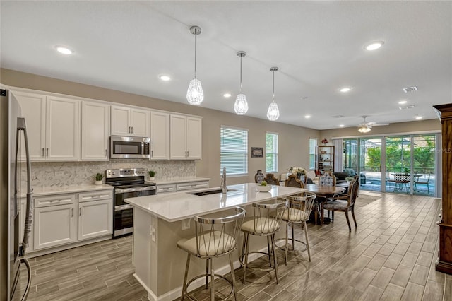 kitchen featuring appliances with stainless steel finishes, an island with sink, decorative light fixtures, and white cabinets