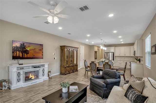 living room with a lit fireplace, visible vents, and light wood-style flooring