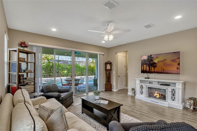 living room featuring a lit fireplace, visible vents, ceiling fan, and wood finish floors