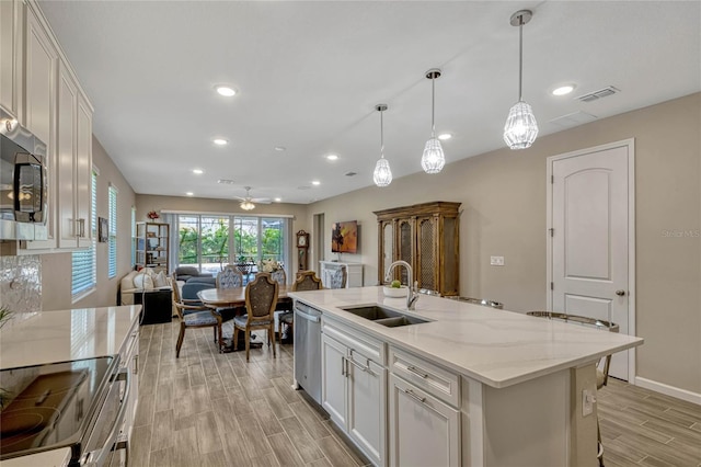 kitchen with a sink, white cabinetry, open floor plan, appliances with stainless steel finishes, and an island with sink