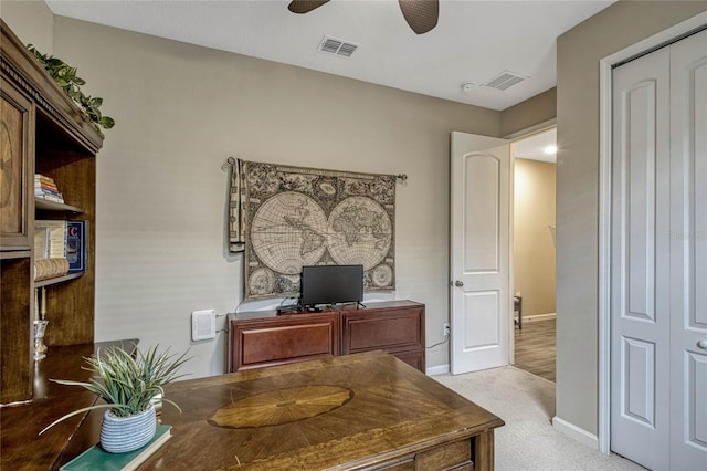 office featuring baseboards, visible vents, a ceiling fan, and light colored carpet