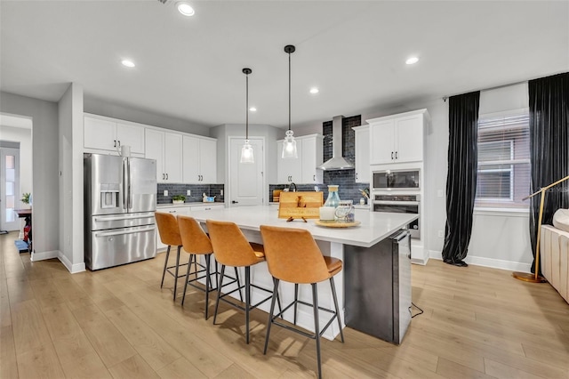 kitchen with wall chimney range hood, a large island with sink, pendant lighting, stainless steel appliances, and white cabinets