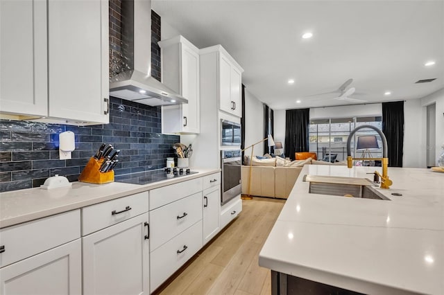 kitchen with wall chimney exhaust hood, sink, white cabinetry, light hardwood / wood-style flooring, and appliances with stainless steel finishes