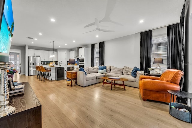 living room with ceiling fan, plenty of natural light, sink, and light wood-type flooring