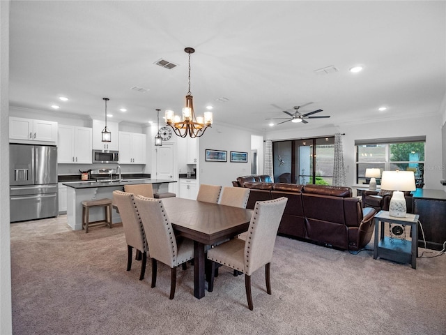 carpeted dining room with sink, ceiling fan with notable chandelier, and ornamental molding