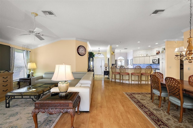 living room featuring crown molding, vaulted ceiling, ceiling fan with notable chandelier, and light wood-type flooring