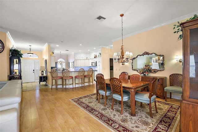 dining area with crown molding, a chandelier, and light wood-type flooring