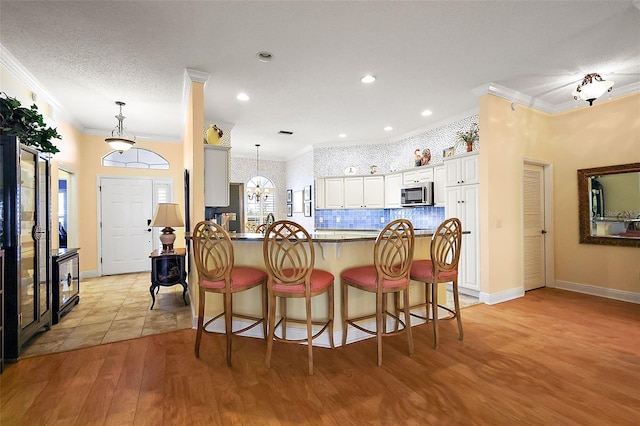 kitchen with white cabinetry, crown molding, light hardwood / wood-style floors, and kitchen peninsula