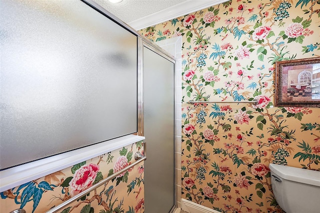 bathroom featuring a shower with door, ornamental molding, toilet, and a textured ceiling